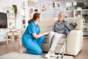 Granny sitting on a couch in a nursing home talking with female nurse.